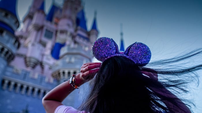 A theme park visitor approaches the Disney castle wearing purple mouse ears.