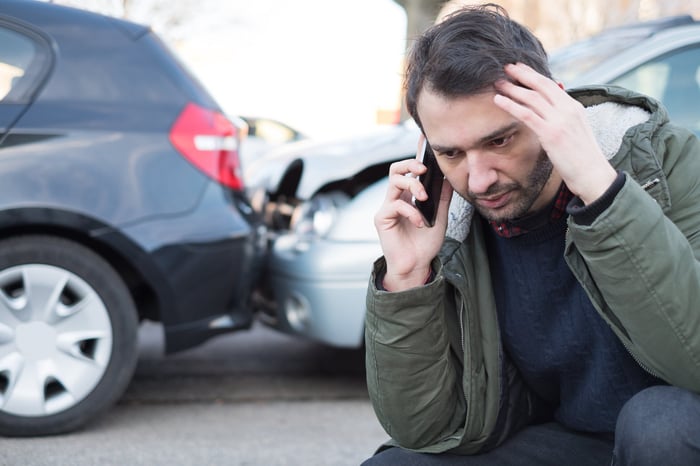 A person is on the phone while standing in front of a car collision.