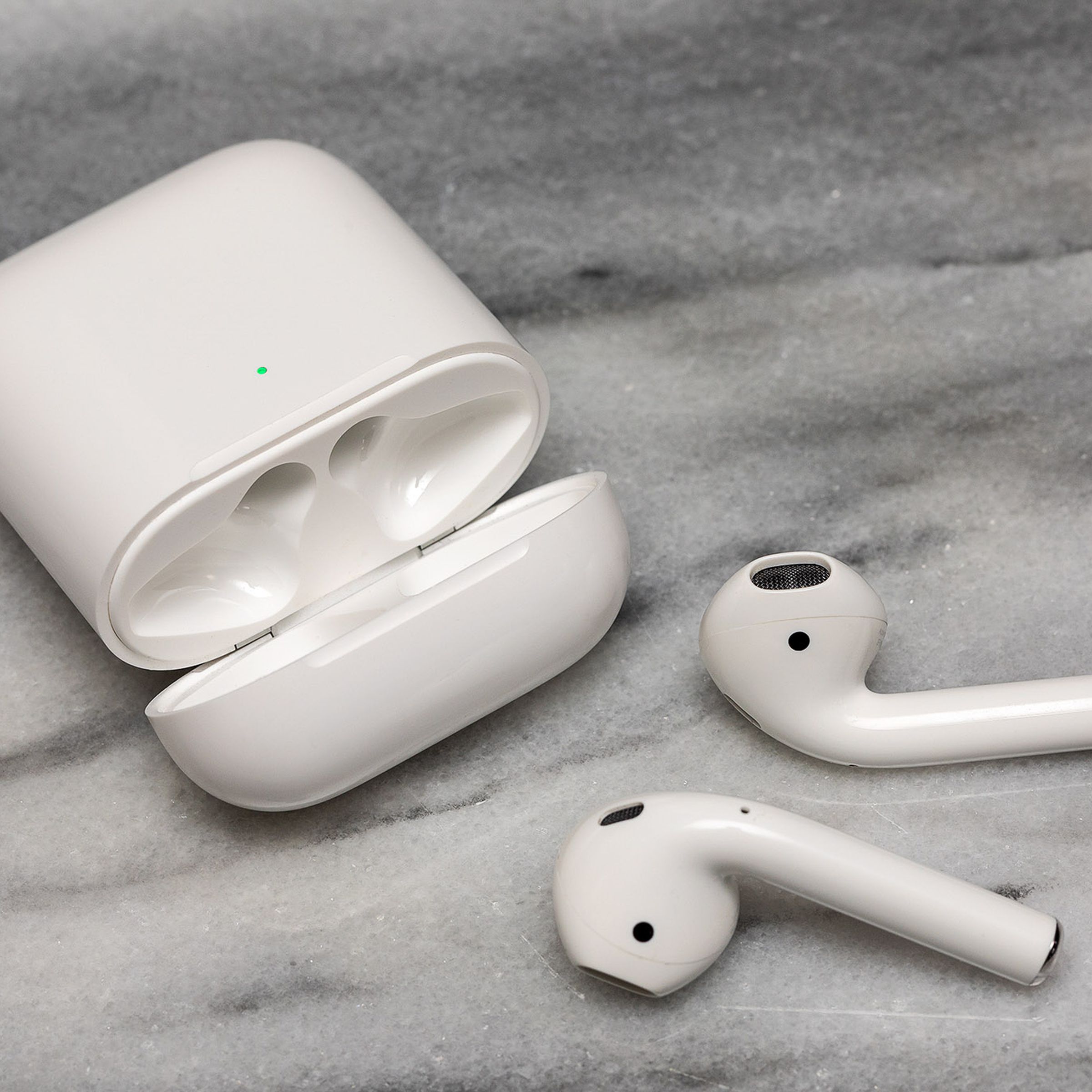 The second-generation AirPods near their charging case on a white surface.