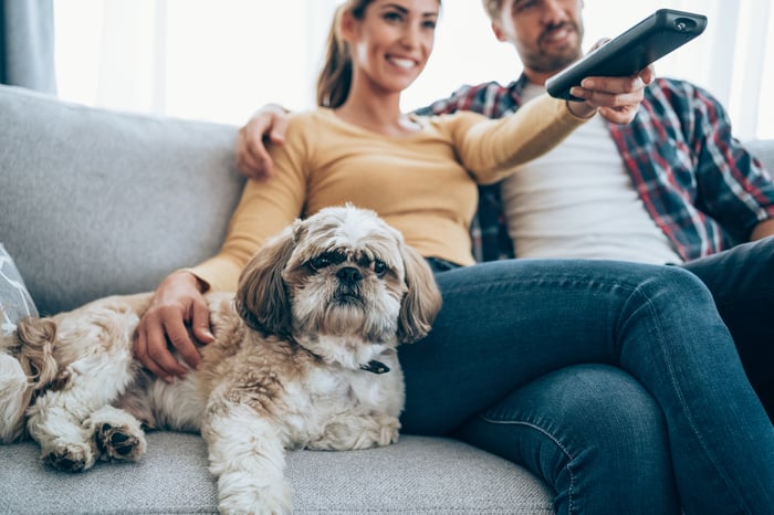A couple watching TV with their dog.