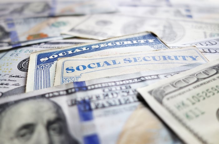 Two Social Security cards surrounded by a messy pile of one hundred dollar bills. 