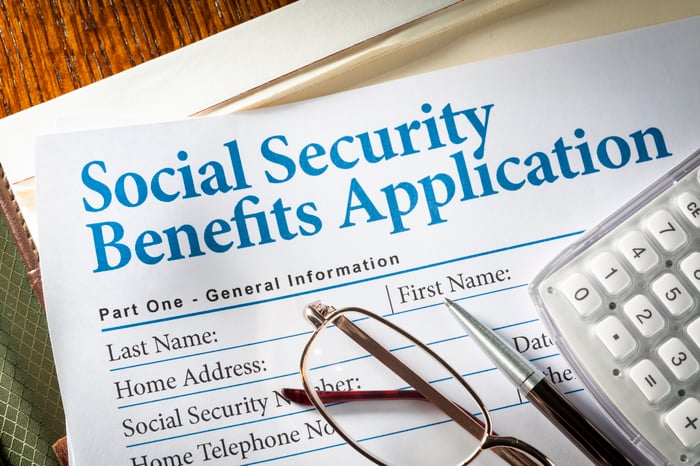 A pair of glasses, a pen, and a calculator sit atop a Social Security benefits application.
