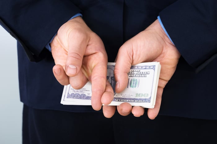 A businessperson holding a stack of one hundred dollar bills behind their back while crossing their fingers.