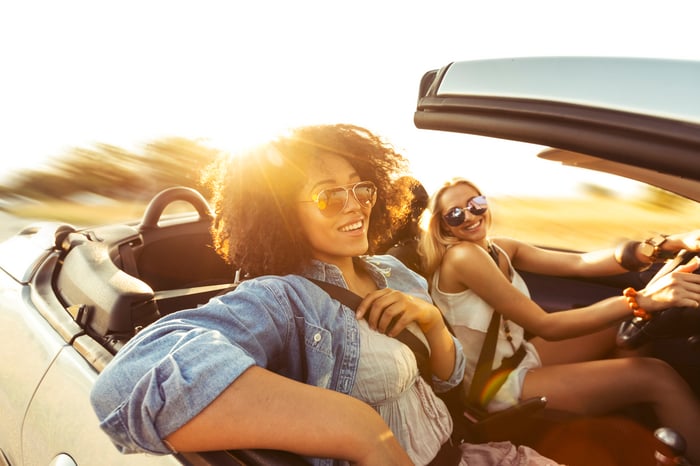 Two people in a car smiling as they drive with the top down.